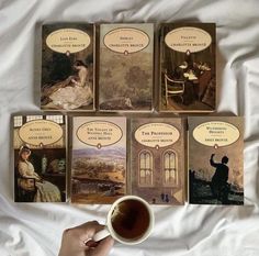 a person holding a cup of coffee in front of four books on a white sheet