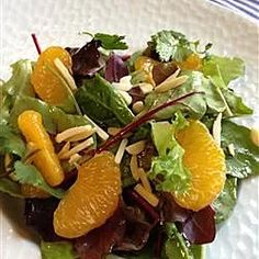 a salad with oranges, almonds and lettuce on a white plate