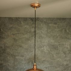 a copper colored light hanging from a ceiling fixture in a room with concrete walls and flooring