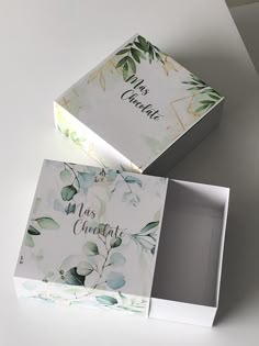 two white boxes with green leaves on them sitting next to each other, one opened and the other closed