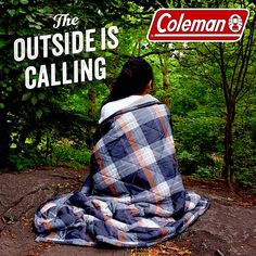 a woman sitting on top of a blanket in the woods under a sign that says, the outside is calling