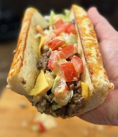 a close up of a person holding a hot dog with toppings in their hand