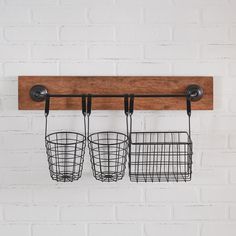 two metal baskets hanging from a wooden shelf on a white brick wall with black hooks