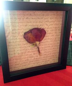 a framed piece of paper with writing on it and a dried flower in the middle