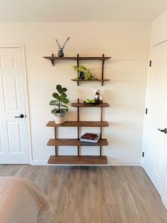 a room with a bed, bookshelf and plant on the wall next to it