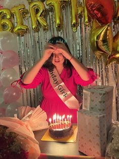 a woman standing in front of a birthday cake with candles on it and presents around her