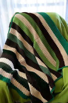 a green and black striped blanket sitting on top of a chair next to a window