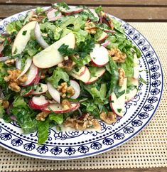 a salad with apples and walnuts in a blue and white plate on a table