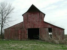 an old red barn sits in the middle of a grassy field with no leaves on it