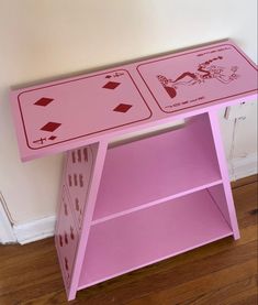 a pink table with two different designs on the top and one shelf below it, in front of a white wall