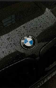 the bmw logo is shown on the front of a black car with rain drops all over it