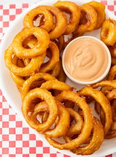 onion rings on a plate with dipping sauce in the middle and checkered tablecloth