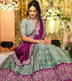 a woman in a green and purple lehenga sitting on a table with flowers