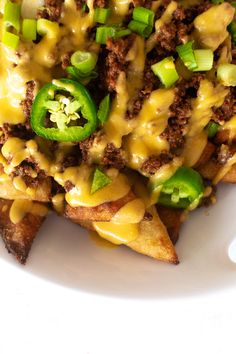 a white plate topped with nachos covered in cheese and green peppers