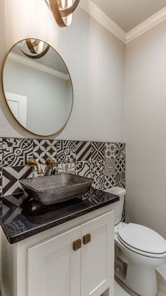 a white toilet sitting next to a bathroom sink under a round mirror on top of a wooden cabinet