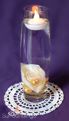 a candle is lit in a glass vase filled with water and floating flowers on a doily