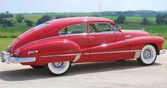 an old red car parked on the side of a road in front of a green field