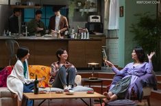 three women sitting on couches in a living room talking to each other and drinking wine