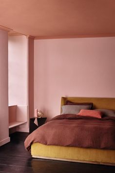 a bedroom with pink walls and a bed in the corner, next to a window