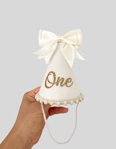 a hand holding a small white hat with the word one on it and a bow at the top