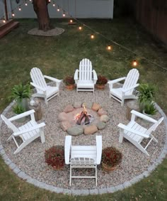 a fire pit surrounded by white chairs and potted plants with lights in the background