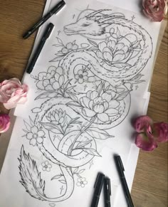 some flowers and pens are on top of a sheet of paper with an image of a dragon