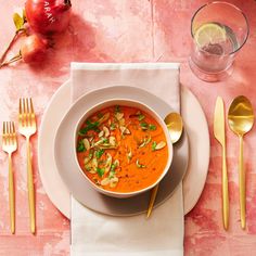 a white plate topped with a bowl of soup next to gold spoons and utensils