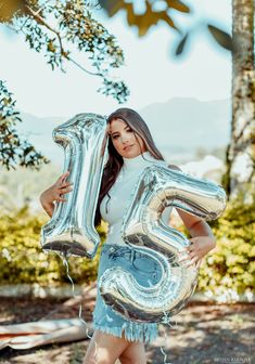 a woman is holding some silver balloons in the shape of the number twenty five,