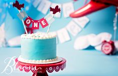 a blue cake with red and white decorations on top is sitting on a table in front of balloons