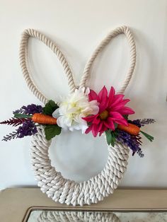 a white rope wreath with flowers and carrots hanging on the wall next to a mirror