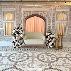 a white couch sitting in front of a wall with flowers on it and two gold lanterns