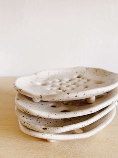 a stack of white ceramic plates sitting on top of a wooden table covered in black speckles