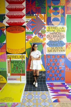 a woman standing in front of a wall covered with colorful posters and letters on it