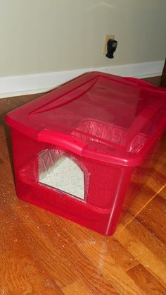 a red plastic litter box sitting on top of a hard wood floor