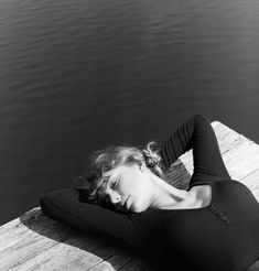 a black and white photo of a woman laying on a dock with her head in her hands