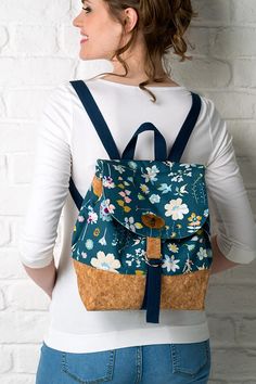 a woman standing in front of a white brick wall wearing a backpack with flowers on it