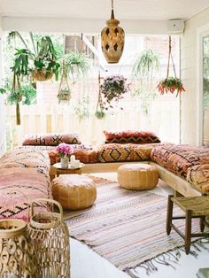 a living room filled with lots of furniture and plants hanging from the ceiling above it