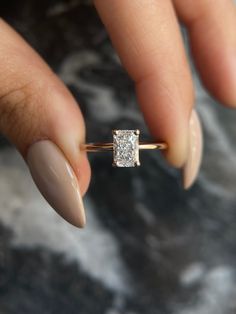 a woman's hand holding an engagement ring with a diamond in the middle, on top of her finger