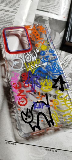 a phone case with graffiti on it sitting on top of a table next to a newspaper