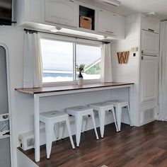 a kitchen with white cabinets and stools in front of a window that looks out onto the water