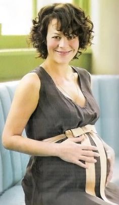 a pregnant woman sitting on a couch with her belly wrapped around her waist and smiling