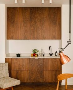 a modern kitchen with wooden cabinets and white counter tops, along with an orange chair