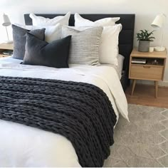 a bed with black and white pillows on top of it next to a night stand