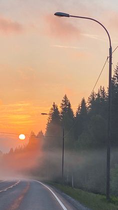 the sun is setting on a foggy road