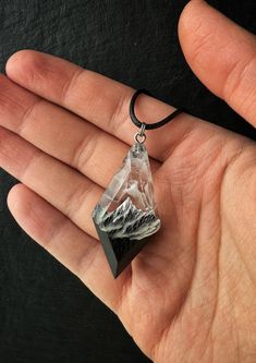 a hand holding a piece of glass in it's palm with mountains on it