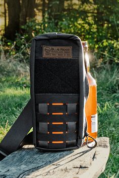 an orange and black bag sitting on top of a wooden bench in the grass next to trees