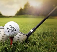 two golf balls and a club on the grass with happy birthday written on them in black ink