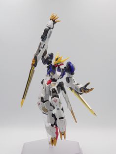 an action figure is posed on a white base with yellow and red accents, holding two swords