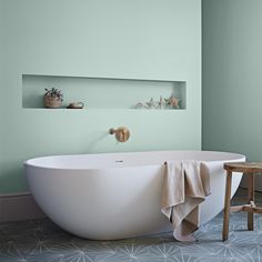 a white bath tub sitting in a bathroom next to a wooden stool and wall mounted shelf