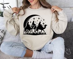 a woman sitting on a couch wearing a sweatshirt with the image of two men riding camels